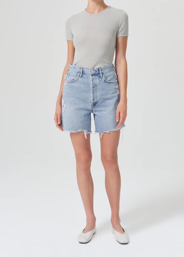Front view of light blue high waisted denim cut off shorts with frayed hem by Agolde..