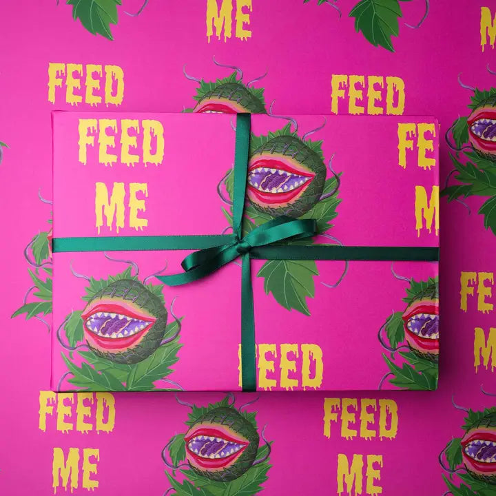 hot pink wrapping paper with Audrey II plant saying Feed Me
